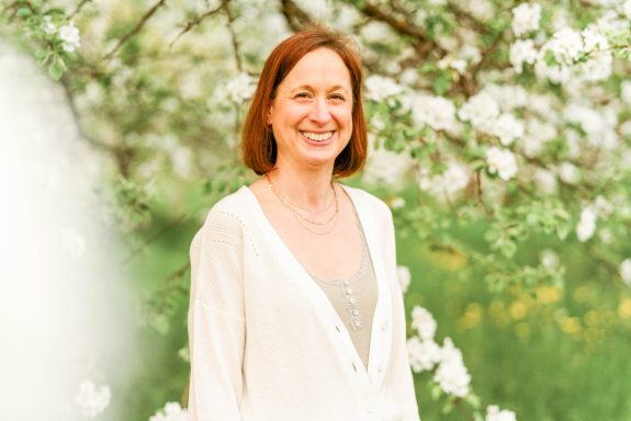 Frau lächelt vor blühenden Bäumen in einem grünen Garten.