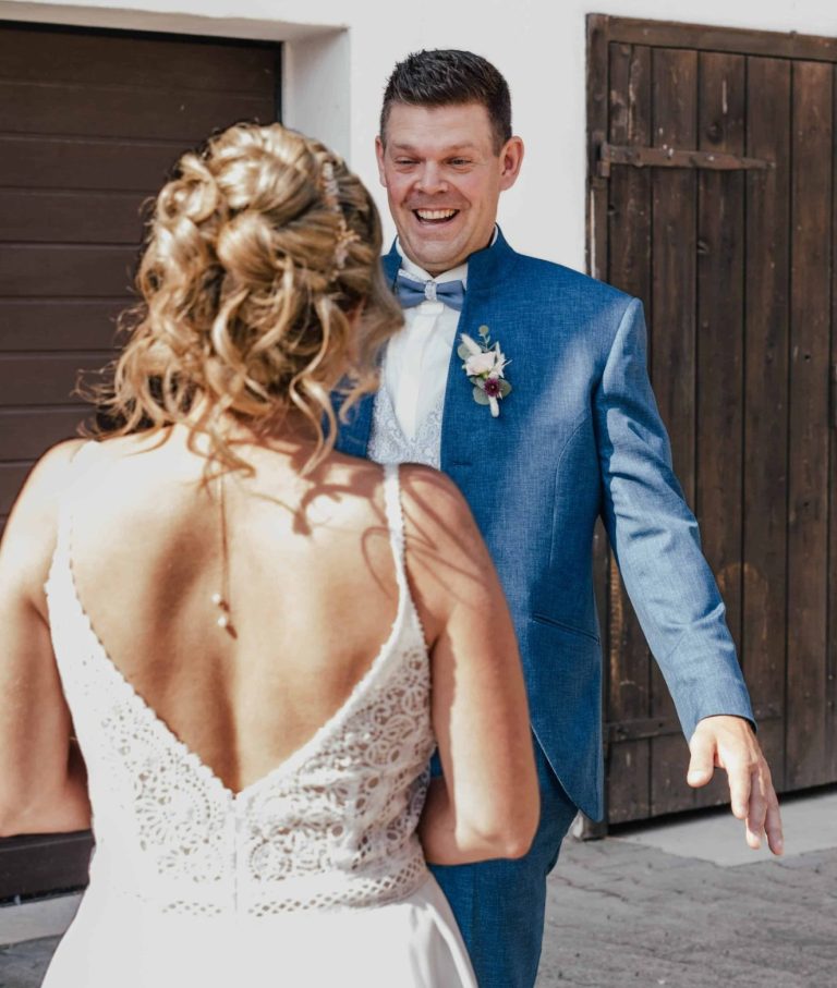Ein Mann in einem blauen Anzug erfreut sich beim Anblick seiner Frau mit Hochzeitskleid - First look.