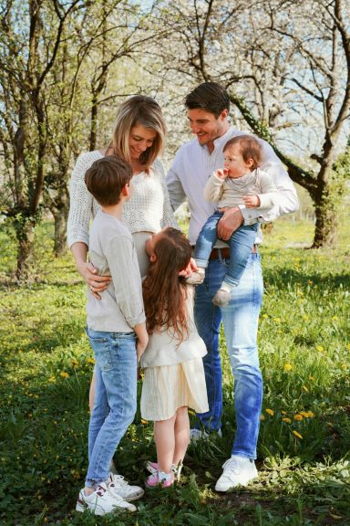 Familie mit zwei Erwachsenen und drei Kindern im Grünen, umgeben von Bäumen und Blumen.