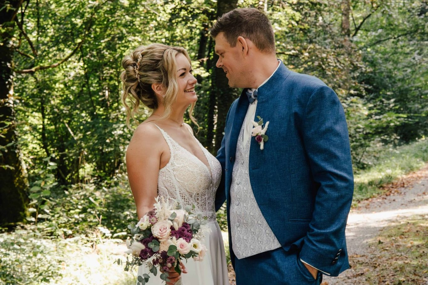 Ein Brautpaar lächelt sich verliebt im Wald an, umgeben von Grün.