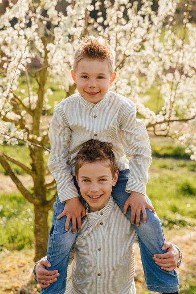 Zwei Jungen stehen vor blühenden Bäumen, der jüngere sitzt auf den Schultern des älteren.