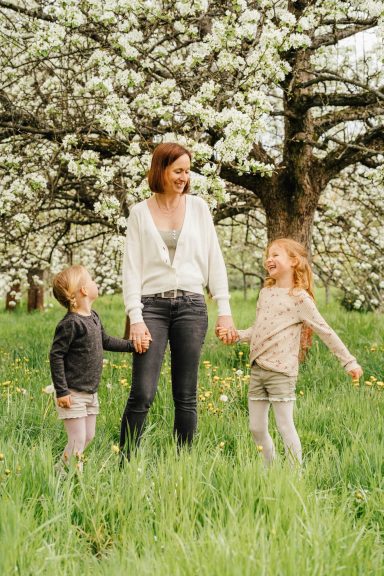 Frau mit zwei Kindern in einer blühenden Obstbaumlandschaft.