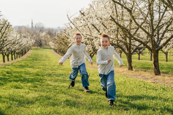 Zwei Jungen laufen fröhlich durch einen blühenden Obstgarten.