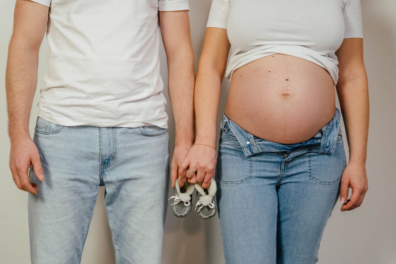 Ein Paar hält Händchen, die Frau ist schwanger und zeigt ihren runden Bauch.