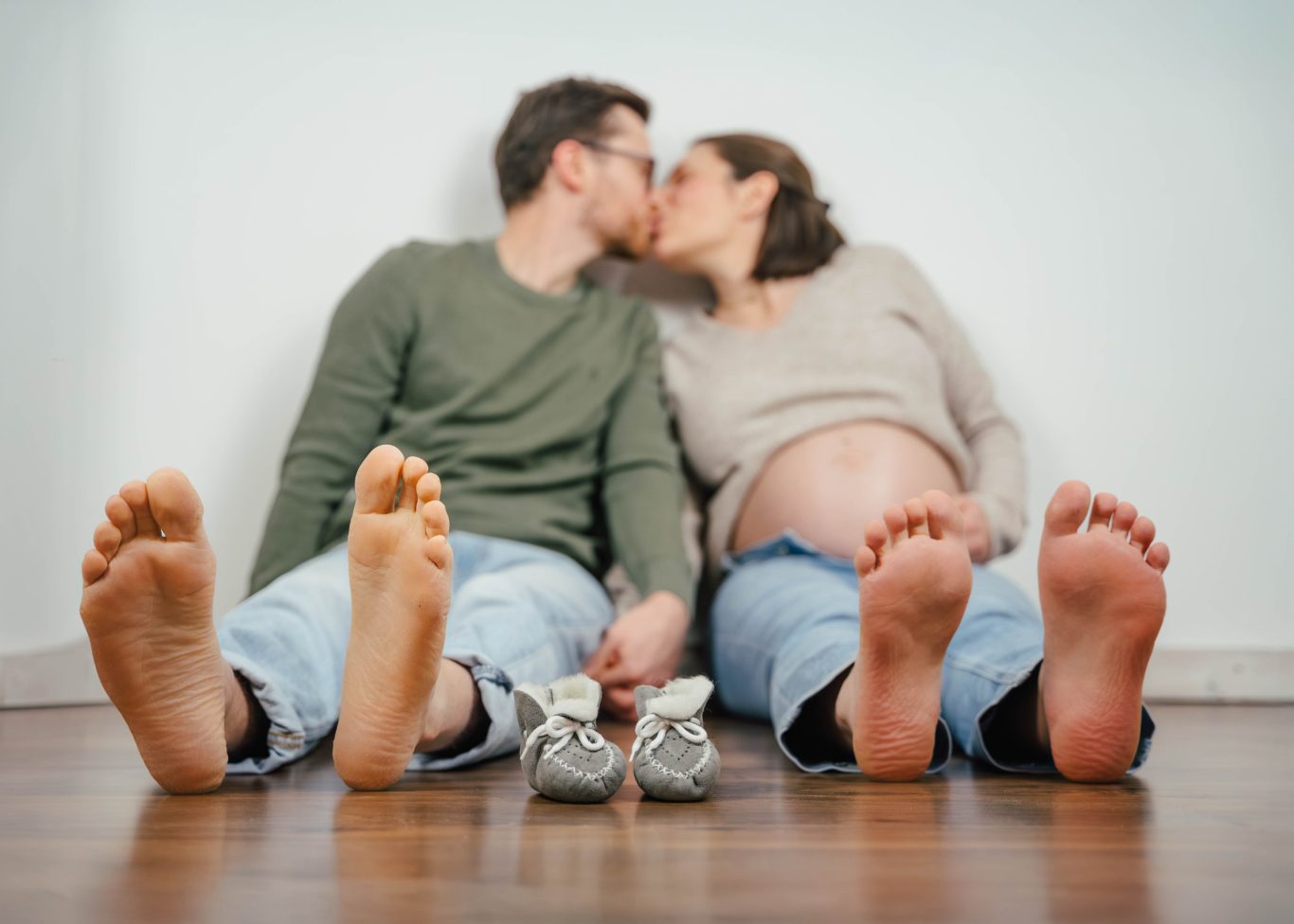 Ein schwangeres Paar küsst sich, während sie barfuß am Boden sitzen.