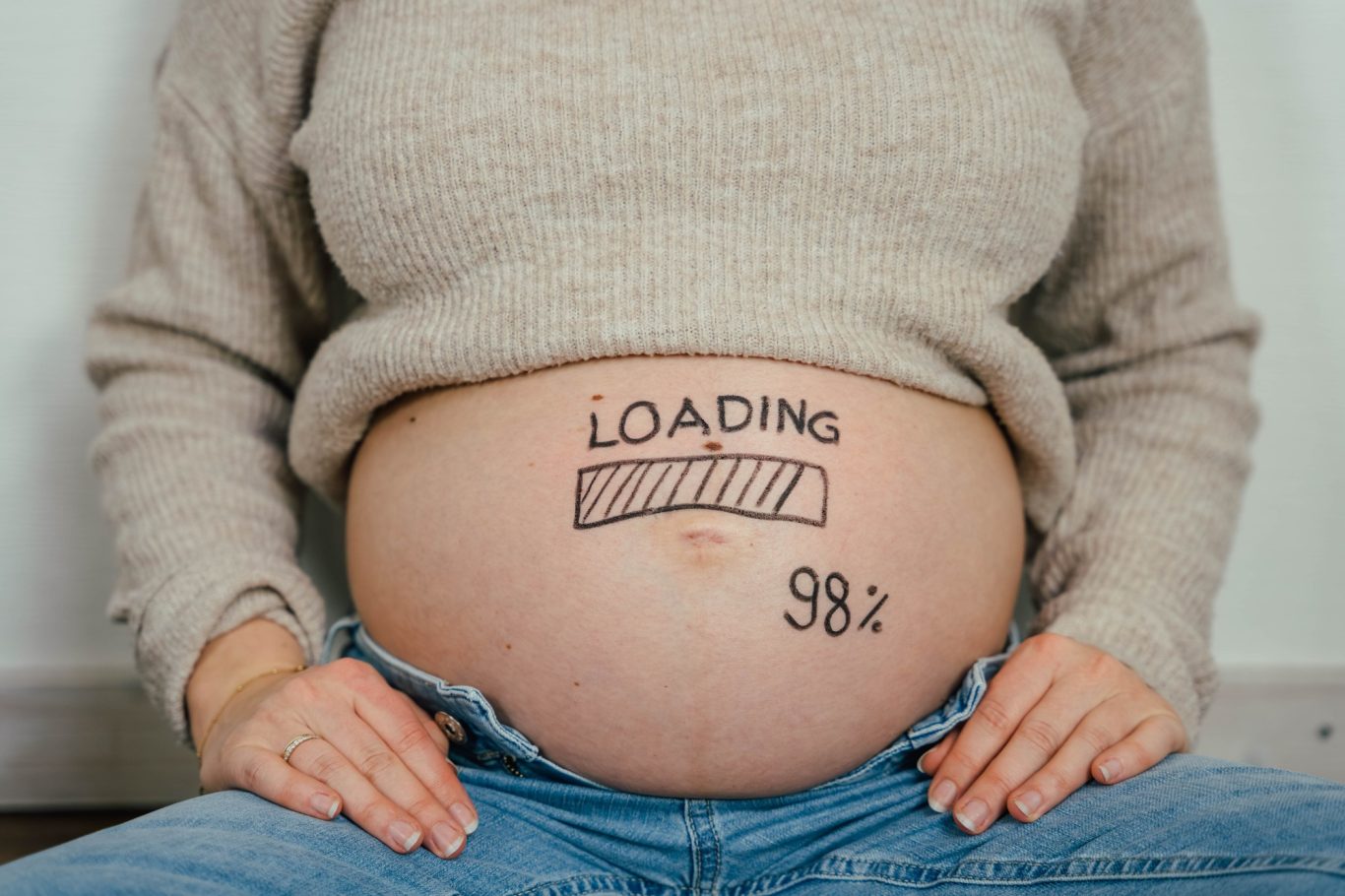 Schwanger Frau, auf deren Bauch "Loading 98%" steht.