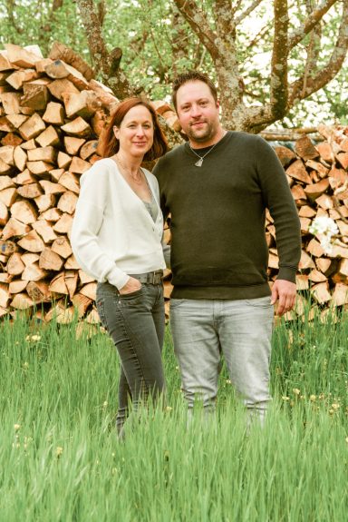Paar steht im Freien vor einem Holzstapel, umgeben von frischem Gras.
