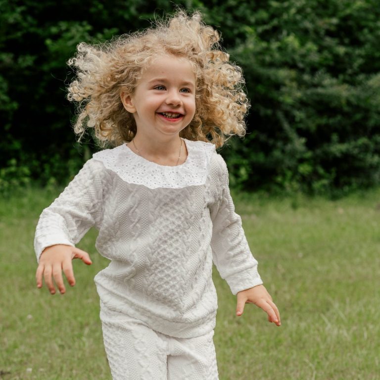 Ein fröhliches Kind mit lockigem Haar, das in einem grünen Feld läuft.