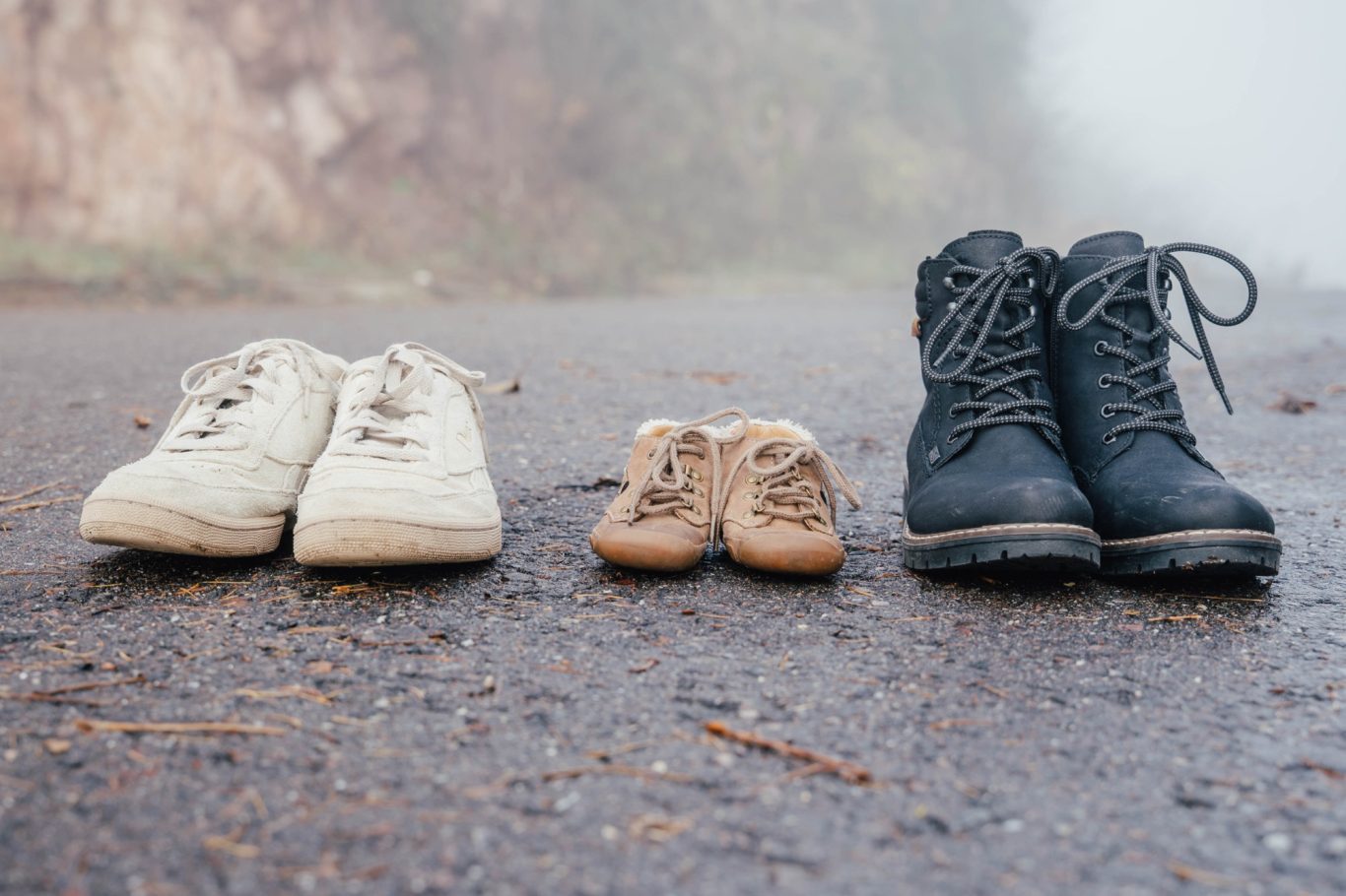 Drei Paar Schuhe unterschiedlicher Größen auf einem nebligen Weg.